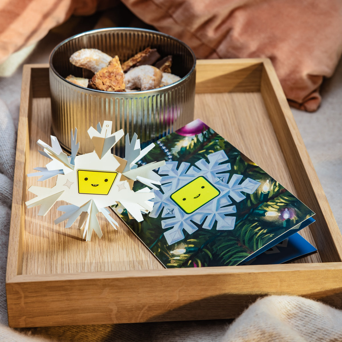 Grußkarte Flocki 3000 auf einem Holztablett, daneben die gefaltete Papierschneeflocke und Weihnachtsplätzchen