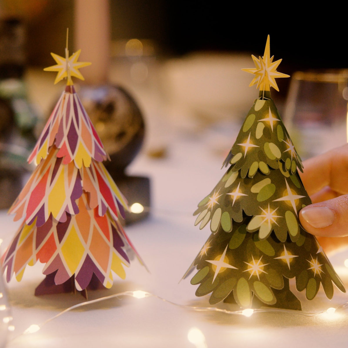 Gefaltete Papier-Weihnachtsbäume von HeyCards und Faltmeister auf dem Festtagstisch mit Lichterkette